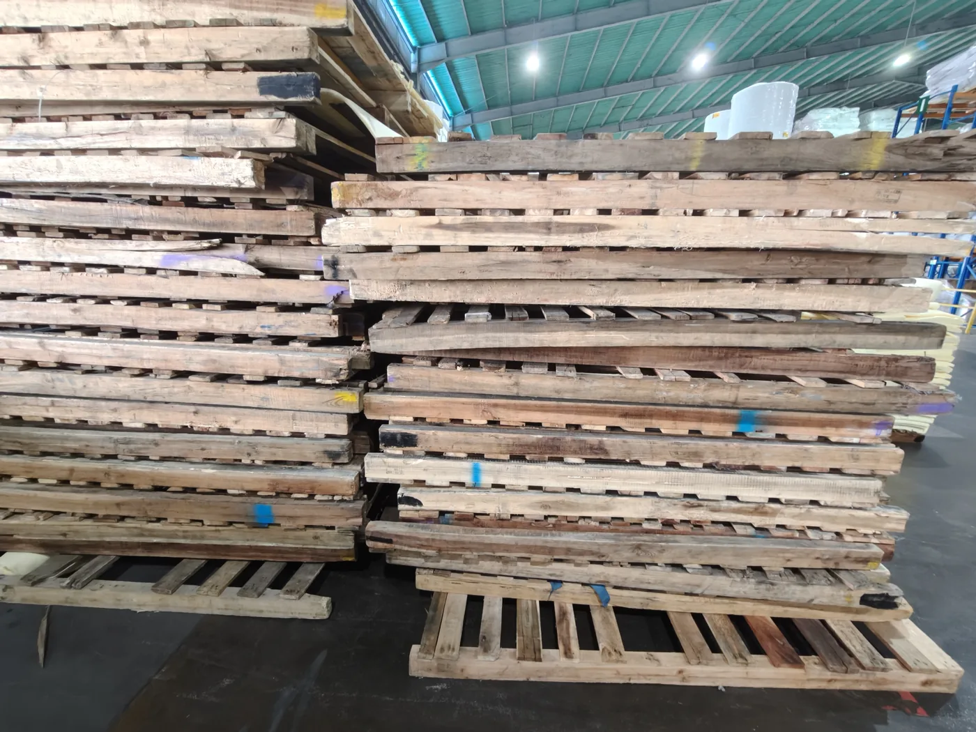 Tall stacks of wooden pallets and timber stored in a manufacturing warehouse.